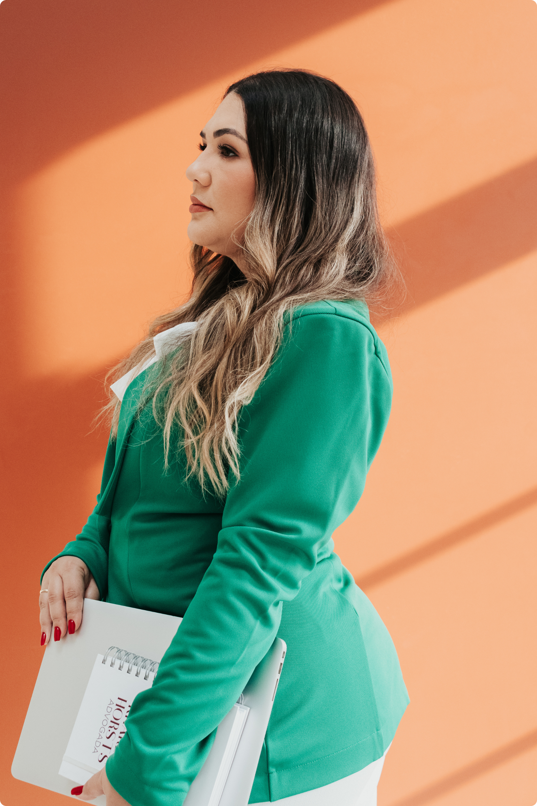 Kharen Horsts de verde, postura confiante junto a parede iluminada, transmitindo credibilidade e profissionalismo.